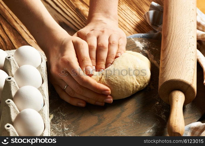 Female hands kneading dough on wooden table