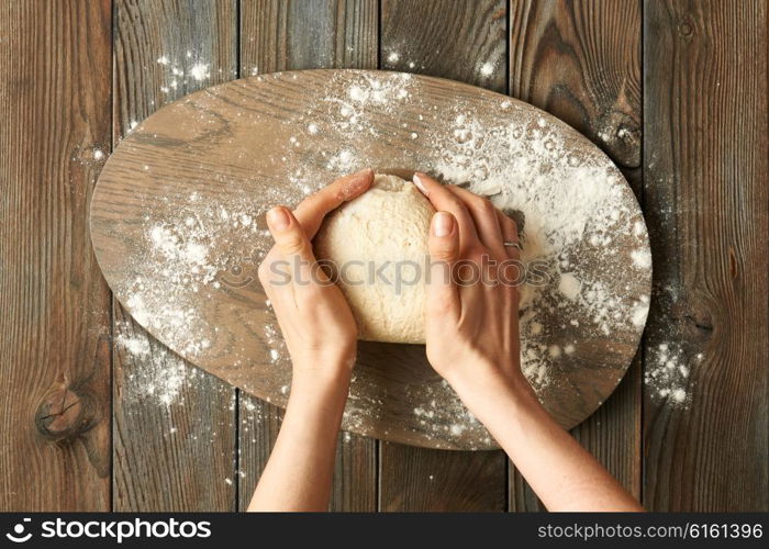 Female hands kneading dough on wooden table