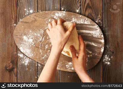 Female hands kneading dough on wooden table