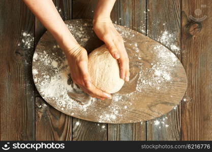 Female hands kneading dough on wooden table