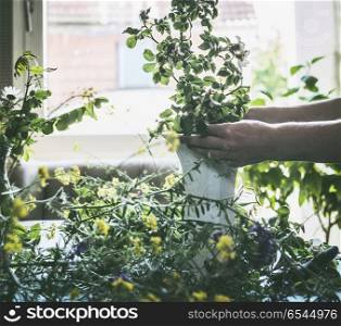 Female hands making summer bouquet with wild flowers on a table in modern living room at window. Summer still life. Cozy home scene