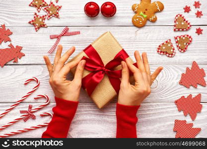 Female hands on christmas gift and homemade gingerbread cookie with handmade decoration on wooden background