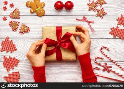 Female hands on christmas gift and homemade gingerbread cookie with handmade decoration on wooden background