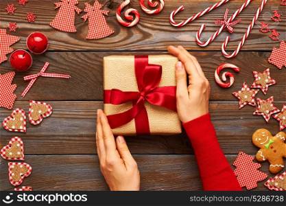Female hands on christmas gift and homemade gingerbread cookie with handmade decoration on wooden background