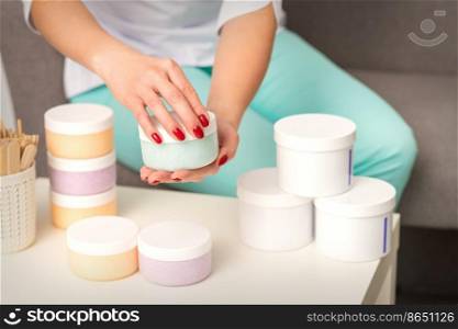 Female hands open a white body cream jar over the table with many jars of cosmetics. Female hands open a white body cream jar over the table with many jars of cosmetics.