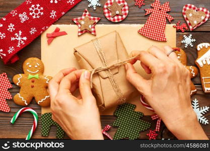 Female hands over christmas gift and homemade gingerbread cookie with handmade decoration on wooden background