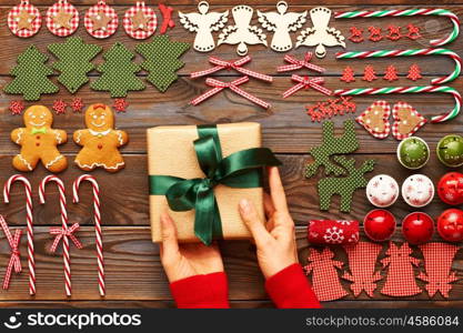 Female hands over christmas gift and homemade gingerbread cookie with handmade decoration on wooden background