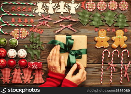 Female hands over christmas gift and homemade gingerbread cookie with handmade decoration on wooden background