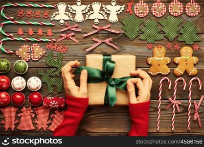 Female hands over christmas gift and homemade gingerbread cookie with handmade decoration on wooden background
