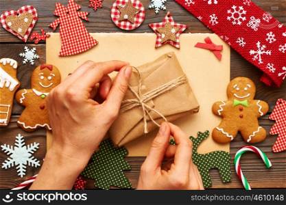 Female hands over christmas gift and homemade gingerbread cookie with handmade decoration on wooden background