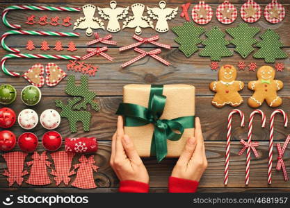 Female hands over christmas gift and homemade gingerbread cookie with handmade decoration on wooden background