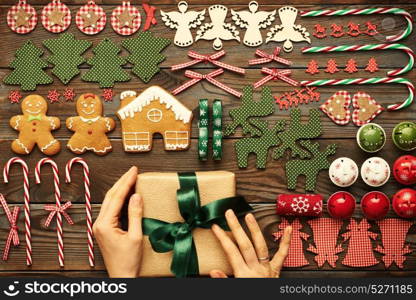 Female hands over christmas gift and homemade gingerbread cookie with handmade decoration on wooden background