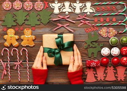 Female hands over christmas gift and homemade gingerbread cookie with handmade decoration on wooden background