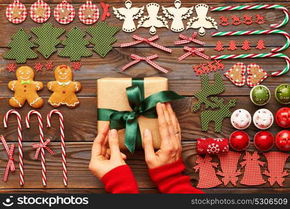 Female hands over christmas gift and homemade gingerbread cookie with handmade decoration on wooden background