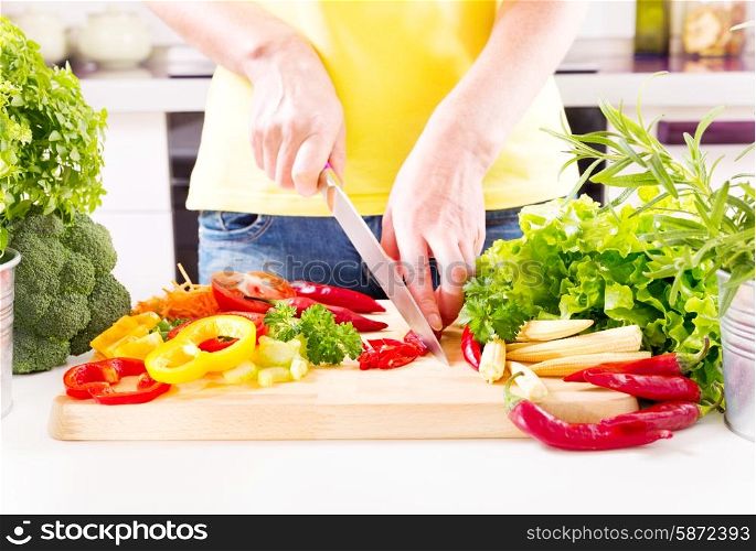 Female hands preparing vegetable salad on wooden board in the kitchen