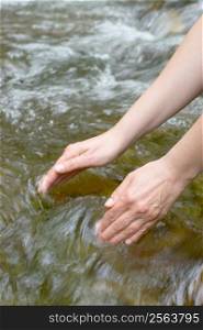 Female hands scooping water from a mountain stream