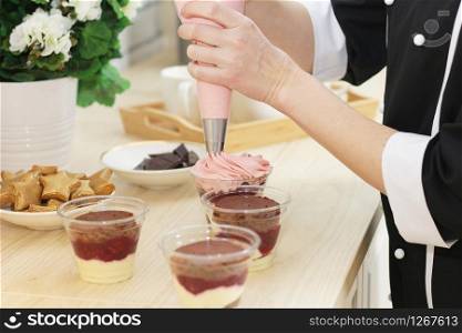 female hands squeeze pink cream from a pastry bag into a glass with dessert.