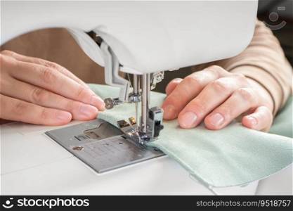 Female hands stitching green fabric on modern sewing machine at workplace in atelier. Women&rsquo;s hands sew pieces of fabric on a sewing machine closeup. Handmade, hobby, small business concept