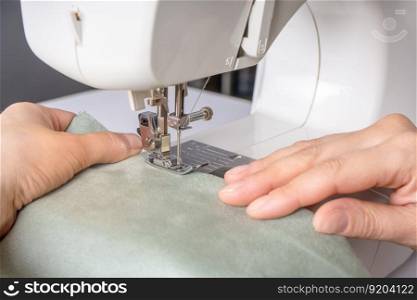 Female hands stitching white fabric on modern sewing machine at workplace in atelier. Women&rsquo;s hands sew pieces of fabric on a sewing machine close-up. Handmade, hobby, small business concept