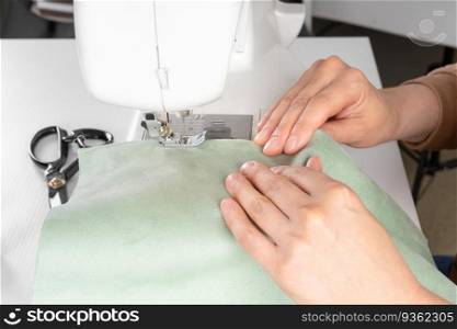 Female hands stitching white fabric on modern sewing machine at workplace in atelier. Women’s hands sew pieces of fabric on a sewing machine closeup. Handmade, hobby, small business concept