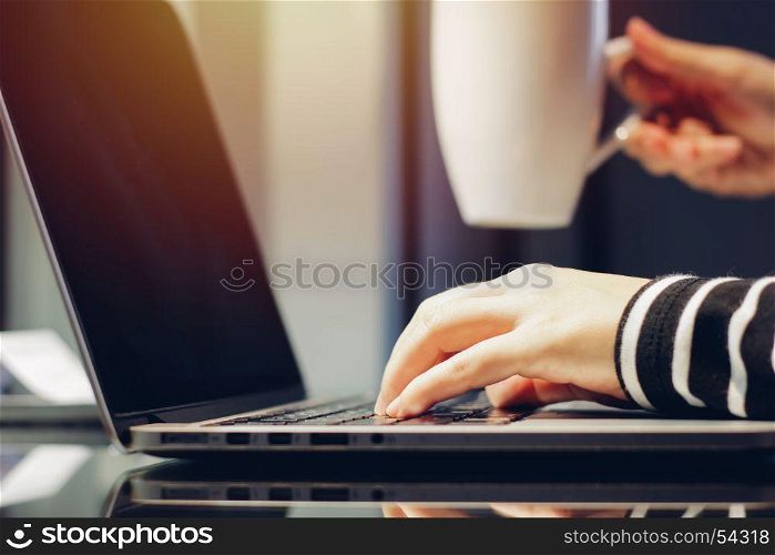 Female hands typing on keyboard of laptop while holding cup of coffee, working at home concept