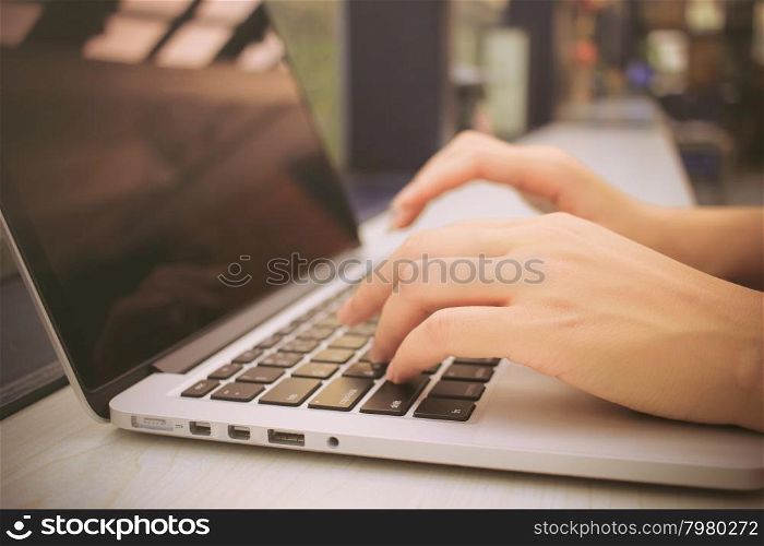 Female hands typing on keyboard of laptop with retro filter effect