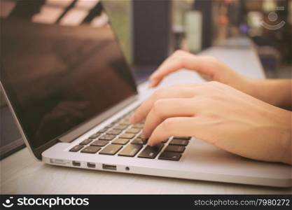 Female hands typing on keyboard of laptop with retro filter effect
