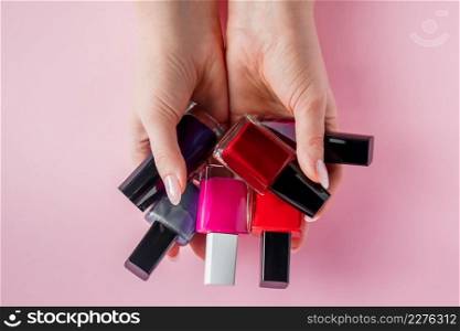 Female hands with bright nail polishes. A group of colored nail enamel on a pink background.. Female hands with bright nail polishes. A group of colored nail enamel on pink background.