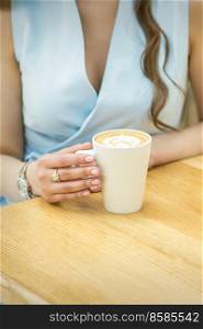 Female hands with cup of coffee on the background of a wooden table in a cafe. Female hands with cup of coffee