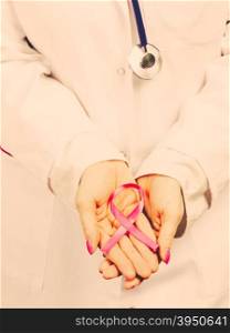 Female hands with pink ribbon. Woman doctor with stethoscope holding pink cancer breast ribbon in hands. Awareness of being sick. Filtered.