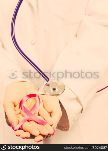 Female hands with pink ribbon. Woman doctor with stethoscope holding pink cancer breast ribbon in hands. Awareness of being sick. Filtered.