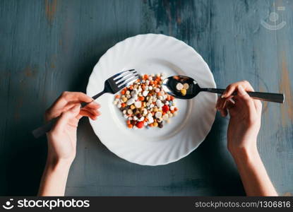 Female hands with spoon and fork, plate full of drugs, top view. Weight loss diet concept