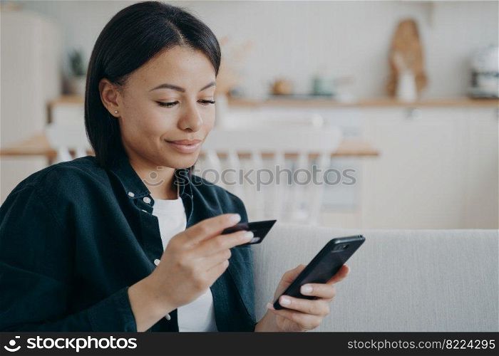 Female holding credit card, smartphone, using online banking services, mobile bank app at home. Modern young woman purchasing, making cashless payment, shopping on internet. E-commerce, e-banking.. Female holding credit card, smartphone, using online banking services, mobile bank app at home