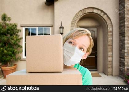Female Holding Delivery or Moving Boxes At Front Door of House Wearing Medical Face Mask.