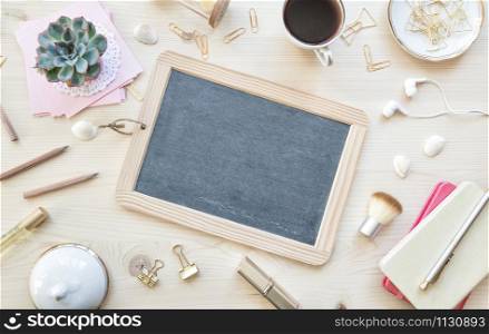 Female home office desk table in pastel tones. Workspace with blank slate, notebooks, cup of coffe and decorations on light wooden background with copy-space. Flat lay, top view