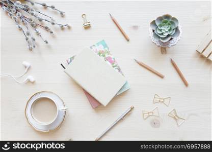 Female home office desk table in pastel tones. Workspace with notebooks, cup of coffe and decorations on light wooden background with copy-space. Flat lay, top view. Female working space in pastel tones