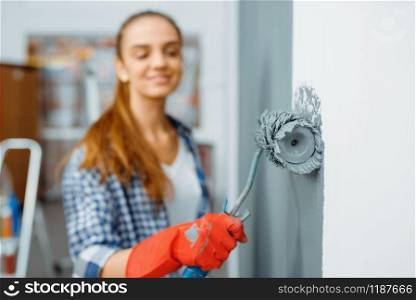 Female house painter in gloves paints the wall. Home repair, laughing woman doing appartment renovation, room renovation. Female house painter in gloves paints the wall