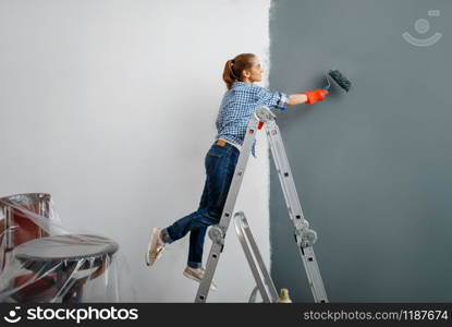 Female house painter in gloves paints the wall. Home repair, laughing woman doing appartment renovation, home renovation. Female house painter in gloves paints the wall