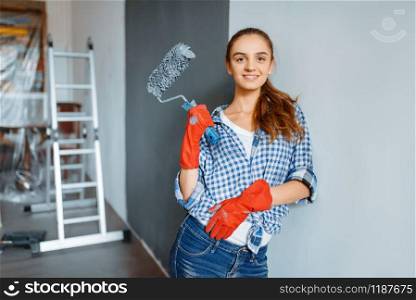 Female house painter in gloves paints the wall. Home repair, laughing woman doing appartment renovation, home renovation. Female house painter in gloves paints the wall