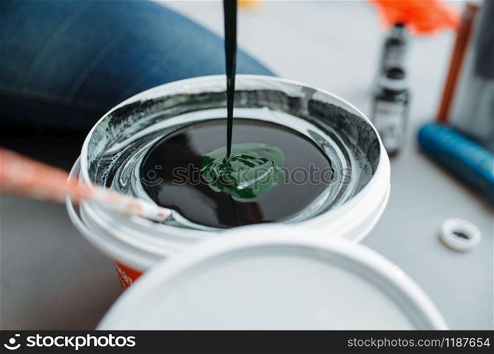Female house painter mixes black and green paints in pail, closeup. Home repair, laughing woman doing appartment renovation, room decoration renovating. Female house painter mixes black and green paints