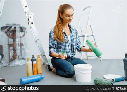 Female house painter mixes paints before painting. Home repair, happy woman doing appartment renovation. Female house painter mixes paints
