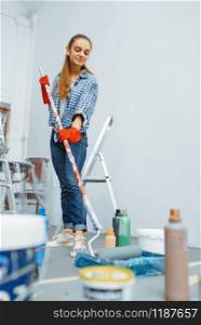Female house painter with paint roller. Home repair, laughing woman doing appartment renovation, room decoration renovating. Female house painter with paint roller