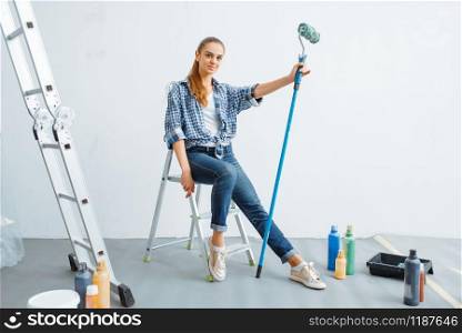Female house painter with paint roller sitting on a ladder. Home repair, happy woman doing appartment renovation. Female house painter sitting on a ladder