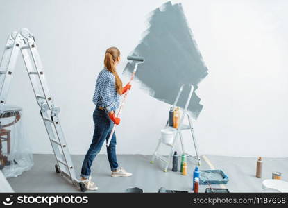 Female house painter with roller paints wall. Home repair, laughing woman doing appartment renovation, room decoration renovating. Female house painter paints wall