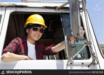 Female industrial worker adjusting mirror while sitting in logging truck