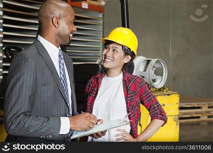 Female industrial worker looking at male inspector as he writes on clipboard