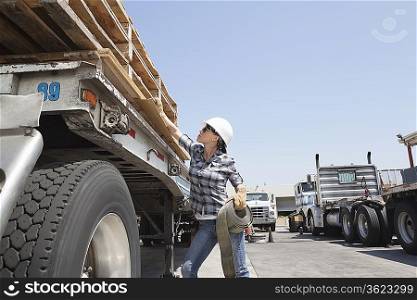 Female industrial worker strapping down wooden planks on logging truck