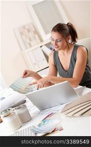Female interior designer working at office holding color swatches with laptop