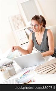 Female interior designer working at office holding color swatches with laptop