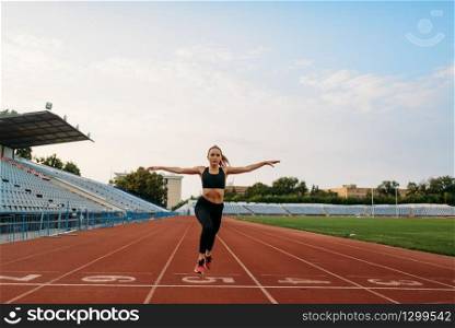 Female jogger in sportswear crosses the finish line, training on stadium. Woman doing stretching exercise before running on outdoor arena